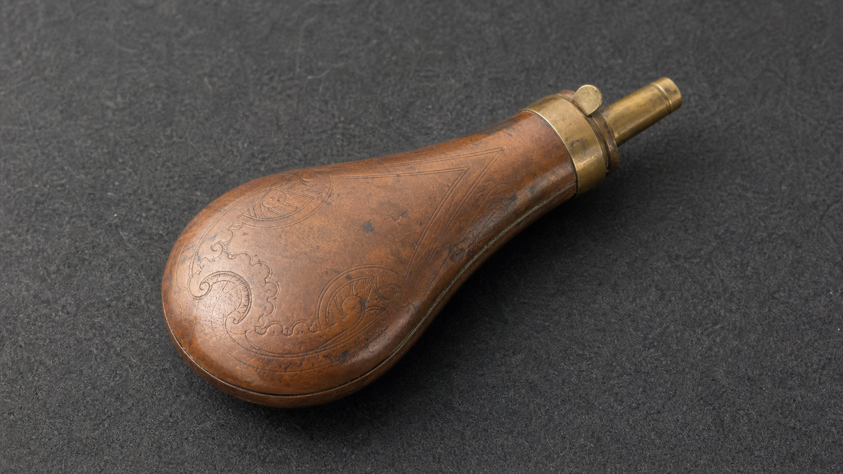 Antique copper powder flask with embossed motif, spout, charger, spring, and seam details