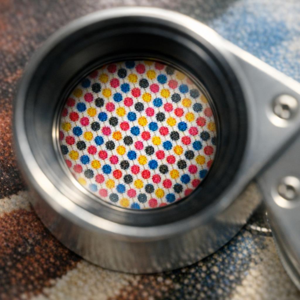 Magnifying glass held over a printed art reproduction revealing tiny CMYK halftone dot patterns invisible to the naked eye