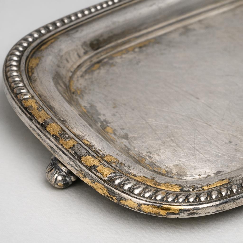 Worn silver-plated serving tray where the thin silver coating has rubbed away at the edges revealing brass-colored base metal underneath